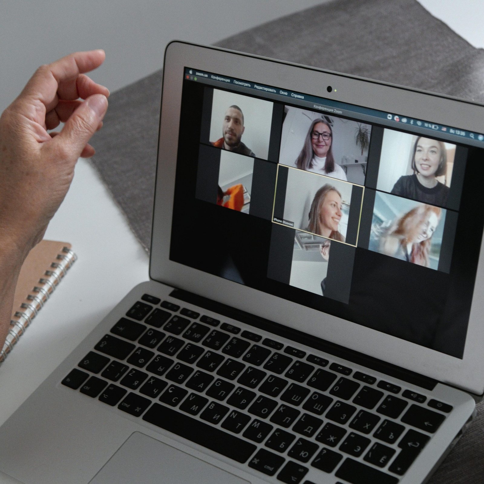 Hands at a laptop showing a group video call in a home office setting.