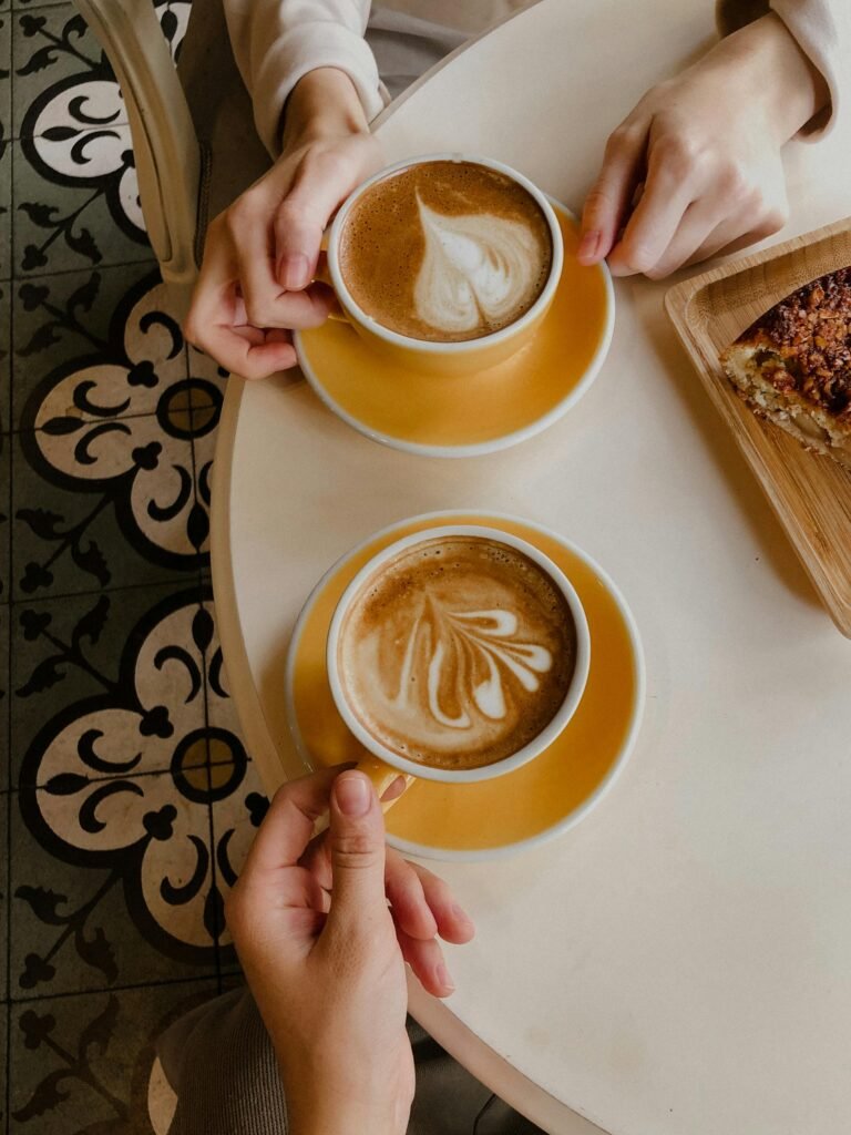Two people enjoy lattes with latte art, sharing a cozy moment at a café.